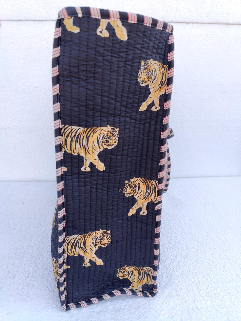 May include: A black quilted tote bag with a pink and white striped trim. The bag features a repeating pattern of orange tigers on a black background.