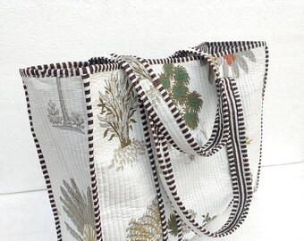 May include: A white tote bag with brown and white striped handles. The bag is made of quilted fabric and features a floral print in shades of green, brown, and white.