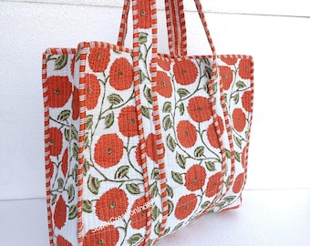 May include: A large white tote bag with orange floral print. The bag has two long straps and is made of quilted fabric.