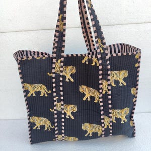May include: A black quilted tote bag with pink and white striped handles. The bag features a repeating pattern of yellow tigers on a black background.