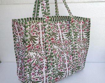 May include: A large green and white tote bag with a floral print. The bag has two long handles and is made of quilted fabric.