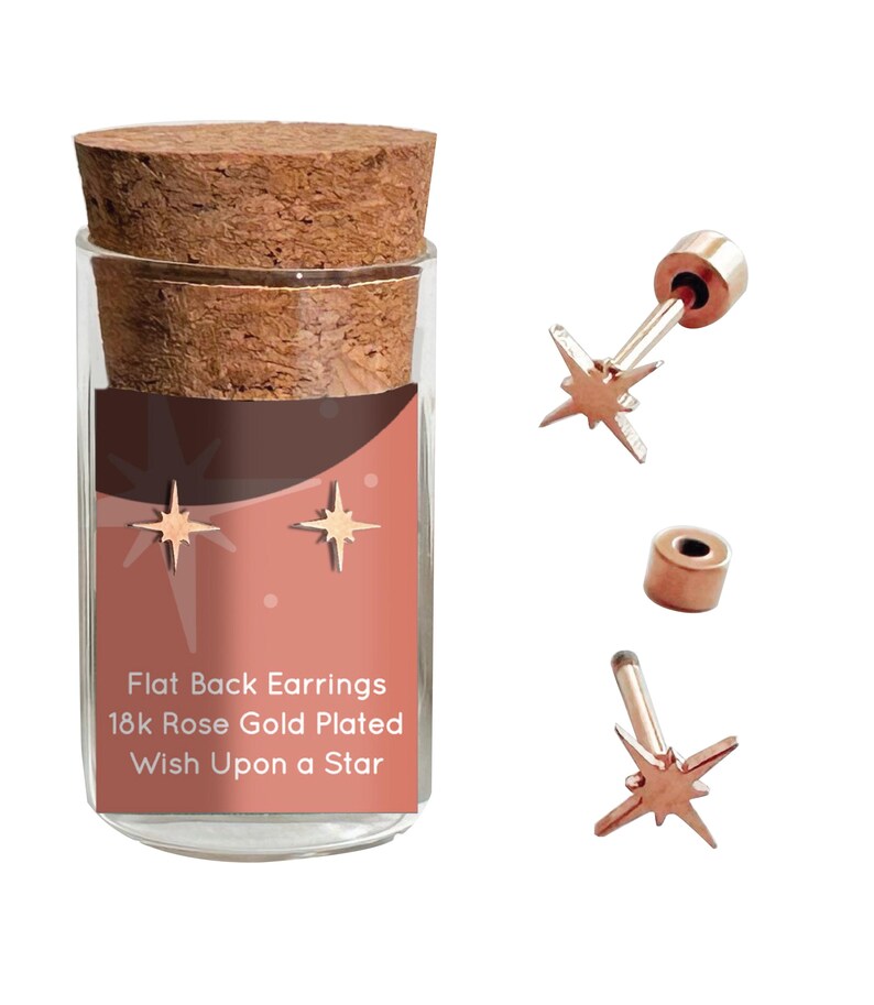 May include: A pair of gold star-shaped earrings in a glass jar with a cork lid. The jar has a label that reads "Flat Back Earrings 18k Rose Gold Plated Wish Upon a Star".