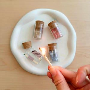 May include: Four small glass bottles with cork tops, each containing a small piece of paper with a star design. One bottle is being lit with a match.