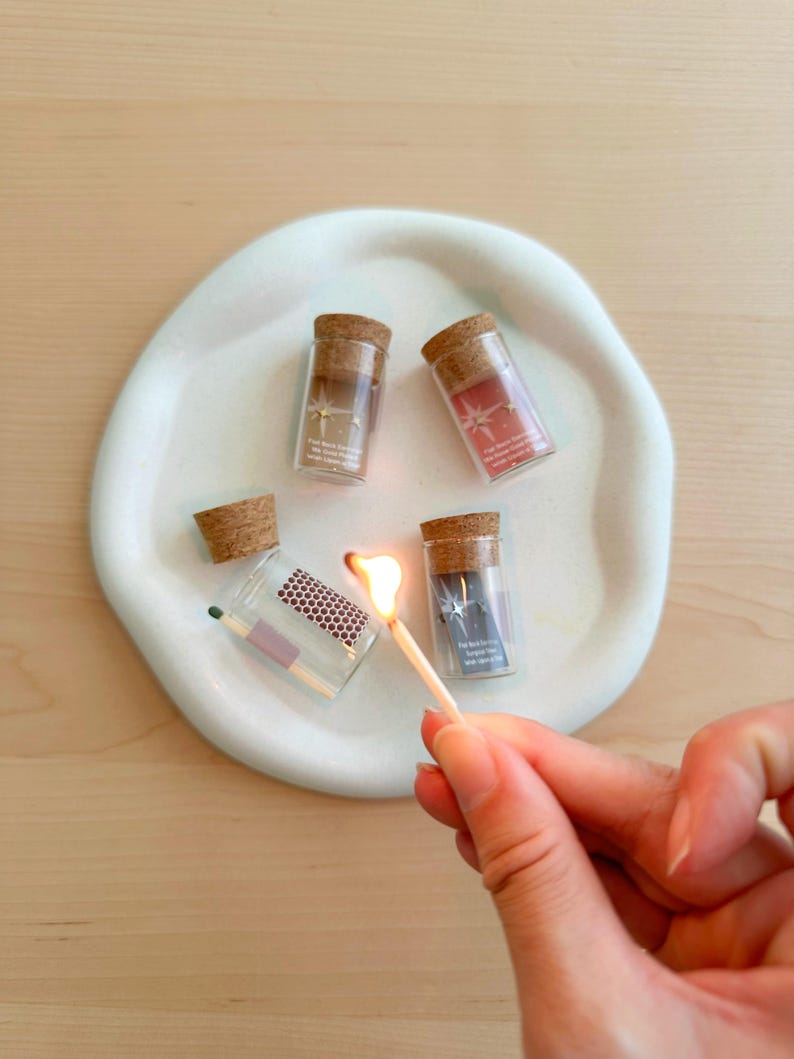 May include: Four small glass bottles with cork tops, each containing a small piece of paper with a star design. One bottle is being lit with a match.