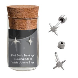 May include: A pair of silver star-shaped earrings in a glass jar with a cork lid. The jar has a black label that reads "Flat Back Earrings Surgical Steel Wish Upon a Star".