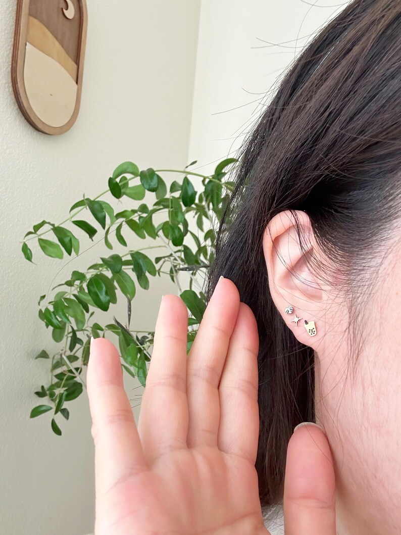 May include: A person's ear with multiple small gold earrings. The earrings are in the shape of a star, a small circle, and a small heart.