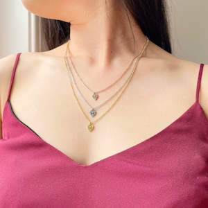 May include: Three layered necklaces with delicate heart pendants. The top necklace is rose gold, the middle is silver, and the bottom is gold.