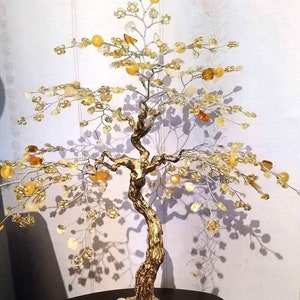 Peut inclure: Une sculpture décorative en forme d'arbre avec un tronc et des branches dorés. Les branches sont ornées de perles jaunes et transparentes en forme de cristaux, ressemblant à des feuilles et des fruits. La base est de couleur marron clair. L'arbre mesure environ 25 cm de haut.