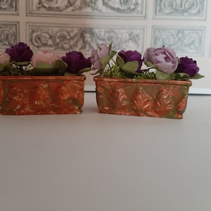 May include: Two terracotta flower boxes with a distressed finish, each filled with purple and pink flowers. The boxes have a decorative design.