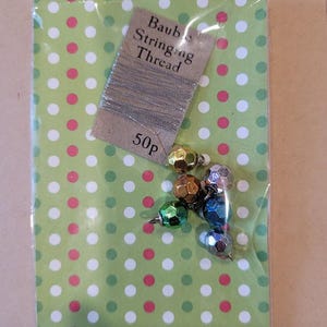May include: A package of silver string and six small, iridescent, multi-colored ornaments. The package is labeled "Bauble Stringing Thread" and "50p".
