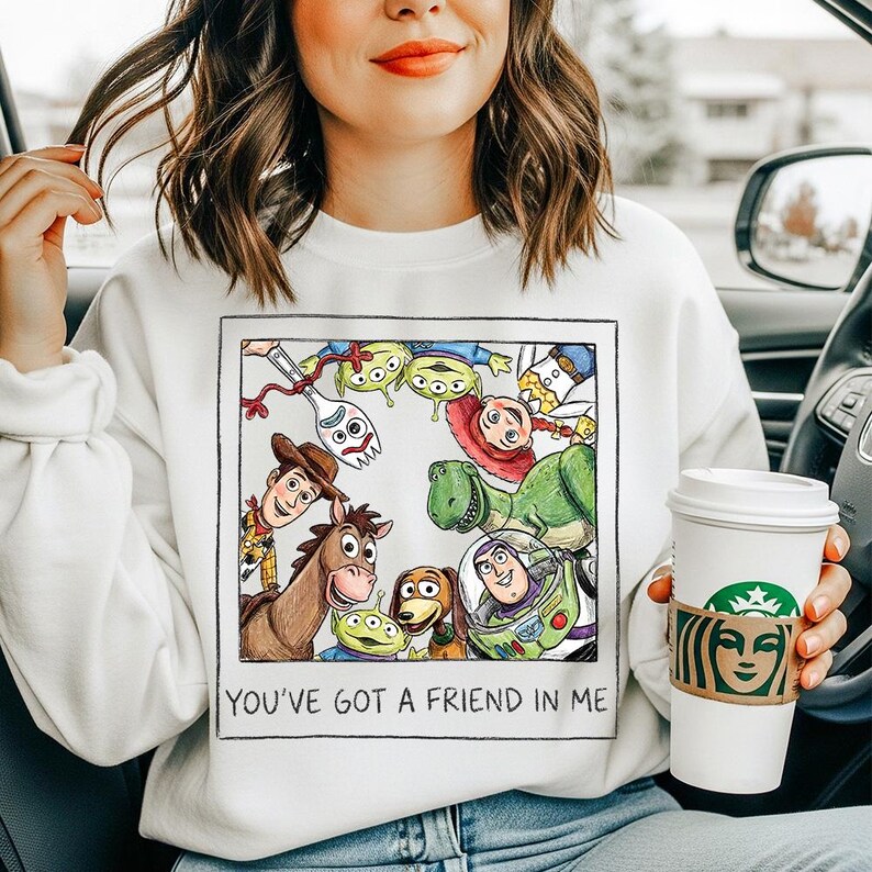 Puede incluir: Sudadera blanca con un gr&aacute;fico colorido de personajes de Toy Story dentro de un borde negro. El texto "YOU'VE GOT A FRIEND IN ME" est&aacute; impreso debajo. La sudadera la lleva una persona.
