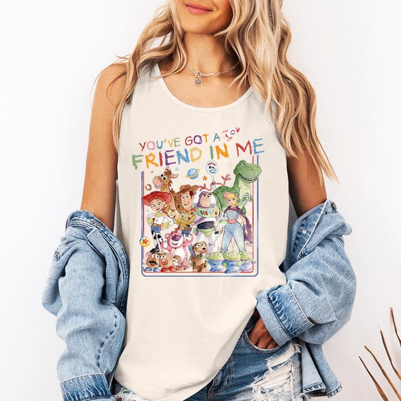 Pu&ograve; includere: Canotta color crema con una grafica colorata dei personaggi di Toy Story. Il testo "YOU'VE GOT A FRIEND IN ME" &egrave; visualizzato sopra i personaggi. Il design include Woody, Buzz Lightyear e altri personaggi del film.