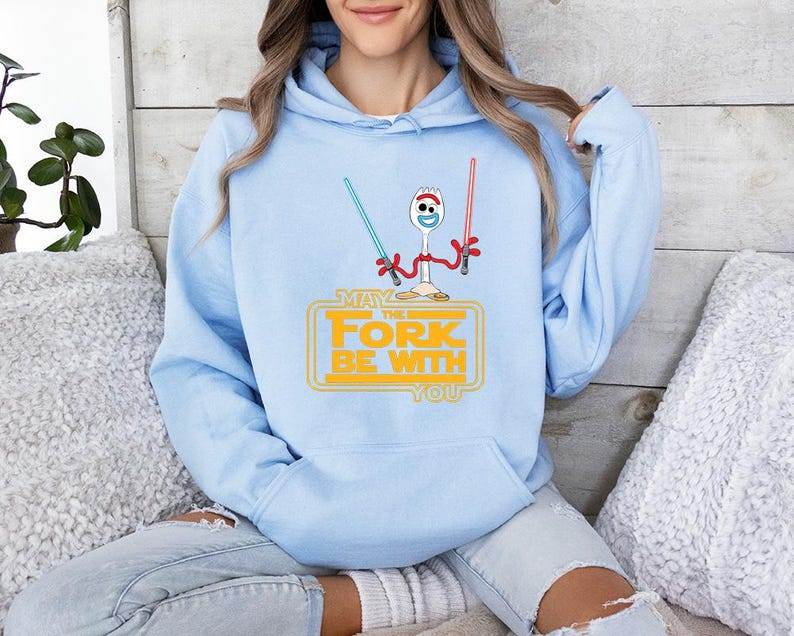 Op de afbeelding: Een lichtblauwe hoodie met een afbeelding van een witte plastic spork met rode pijpenrager-armen die een blauw en een rood lichtzwaard vasthoudt. Onder het figuur staat de gele tekst: MAY THE FORK BE WITH YOU.