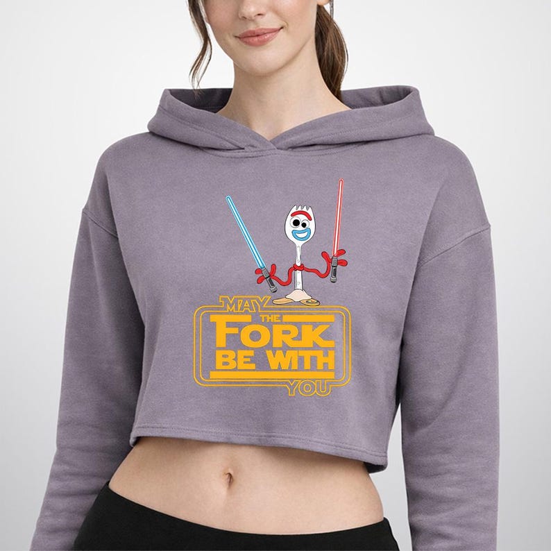 Puede incluir: Una sudadera corta de color malva con un gr&aacute;fico de un personaje spork blanco que sostiene un sable de luz azul y otro rojo. Debajo del personaje, el texto amarillo dice MAY THE FORK BE WITH YOU, dentro de un marco rectangular redondeado.