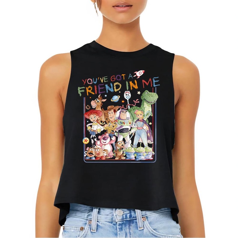 Puede incluir: Top corto sin mangas negro con un gr&aacute;fico colorido de personajes de la pel&iacute;cula Toy Story. El texto "YOU'VE GOT A FRIEND IN ME" est&aacute; impreso encima del gr&aacute;fico. La parte superior la lleva una persona.