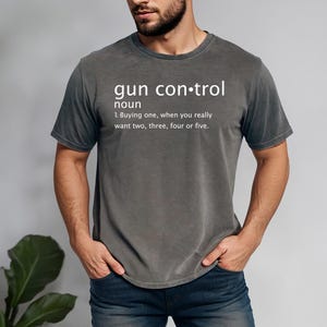 May include: A dark gray t-shirt with a white graphic print that reads "gun control noun 1. Buying one, when you really want two, three, four or five."