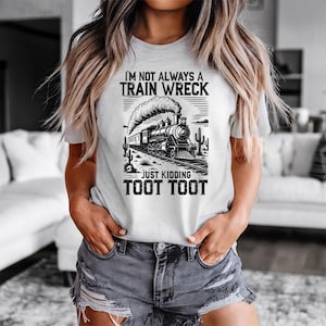 May include: A light gray t-shirt with a black and white graphic of a train and the text "I'M NOT ALWAYS A TRAIN WRECK JUST KIDDING TOOT TOOT". The design includes a train, cacti, and a desert landscape.