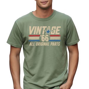 Puede incluir: Camiseta verde salvia con el texto "VINTAGE '66 ALL ORIGINAL PARTS" en un estilo retro desgastado. El dise&ntilde;o incluye una estrella azul y rayas rojas y azules, evocando una est&eacute;tica vintage cl&aacute;sica. La camiseta es de cuello redondo.