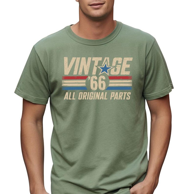 Puede incluir: Camiseta verde salvia con el texto "VINTAGE '66 ALL ORIGINAL PARTS" en un estilo retro desgastado. El dise&ntilde;o incluye una estrella azul y rayas rojas y azules, evocando una est&eacute;tica vintage cl&aacute;sica. La camiseta es de cuello redondo.