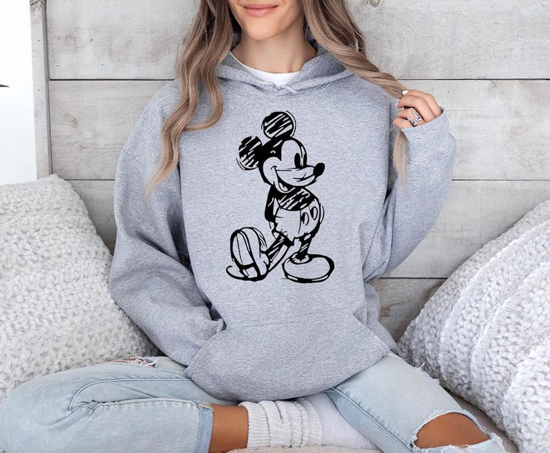 May include: A light gray hooded sweatshirt featuring a black and white sketch of Mickey Mouse. The cartoon character is depicted in a classic pose, with his hands behind his back. The sweatshirt has a drawstring hood and a kangaroo pocket.