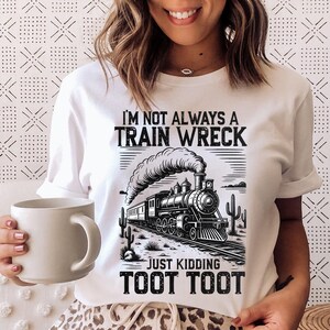 May include: White t-shirt with a black and white graphic of a vintage train, smoke, and desert cacti. The text reads "I'M NOT ALWAYS A TRAIN WRECK, JUST KIDDING, TOOT TOOT."