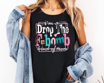 May include: Black tank top with the text "I'm a Drop The F-bomb kind of mom" in pink, white, and teal. The text is inside a pink rectangular frame. The tank top is sleeveless.
