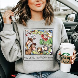 Puede incluir: Sudadera gris con un estampado colorido de personajes de Toy Story. El gr&aacute;fico est&aacute; enmarcado con el texto "YOU'VE GOT A FRIEND IN ME". La sudadera es de cuello redondo.
