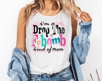 May include: White tank top with the text "I'm a Drop The F Bomb kind of mom" in black, pink, teal, and orange. The text is inside a pink square. The model is wearing a denim jacket and blue jeans.