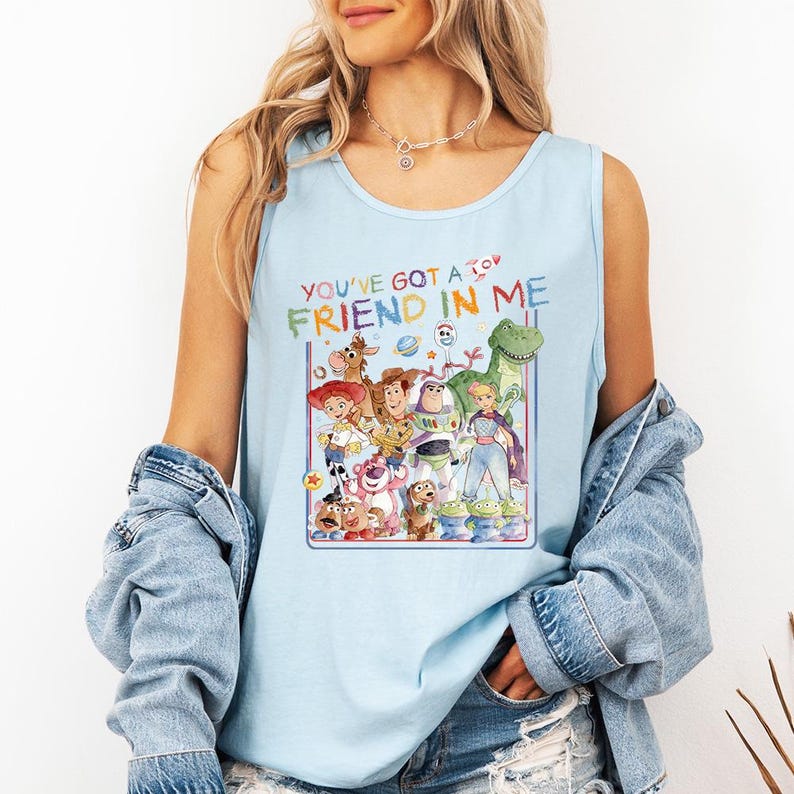Pu&ograve; includere: Canotta azzurra con una grafica colorata dei personaggi del film Toy Story. Il testo "YOU'VE GOT A FRIEND IN ME" &egrave; sopra la grafica. La canotta &egrave; senza maniche e ha uno scollo tondo.