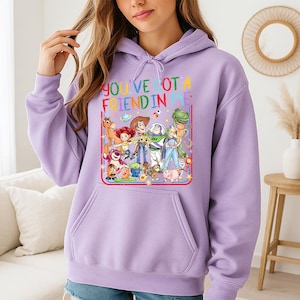 May include: A light purple hooded sweatshirt featuring a graphic print of various animated characters from the Toy Story franchise. The text "YOU'VE GOT A FRIEND IN ME" is printed in colorful letters above the characters, and a kangaroo pocket is visible.