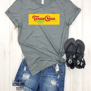 May include: Gray t-shirt with a yellow and red graphic that says "Texas Chica con Lima". The graphic features a lime wedge.