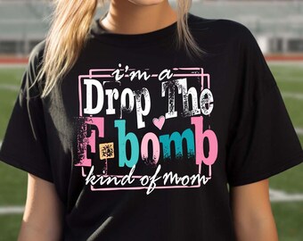 May include: Black t-shirt with the text "I'm a Drop The F-bomb kind of mom" in white, pink, and teal lettering. The design includes a heart and a small square graphic. The shirt is a casual style.