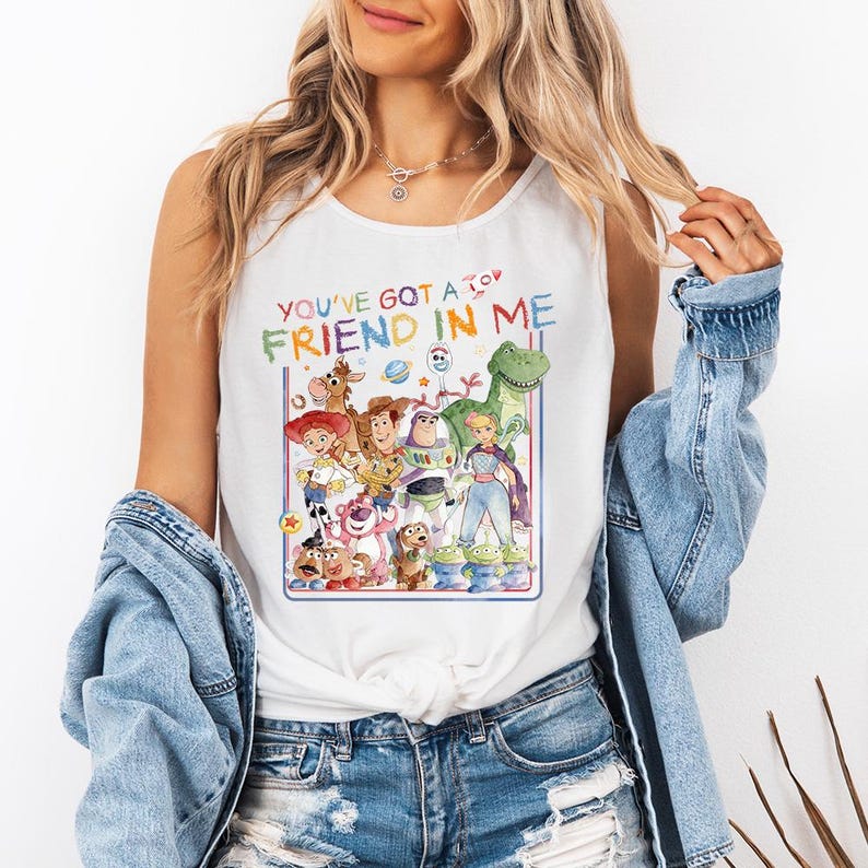 Pu&ograve; includere: Canotta bianca con una grafica colorata dei personaggi di Toy Story. Il testo "YOU'VE GOT A FRIEND IN ME" &egrave; visualizzato sopra i personaggi. Il design include Woody, Buzz Lightyear e altri personaggi.