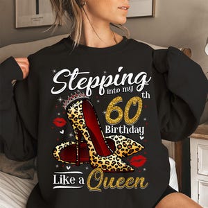 May include: Black sweatshirt with a graphic design featuring a high-heeled shoe with a leopard print, a crown, and the text "Stepping into my 60th Birthday Like a Queen". The number 60 is in gold glitter.