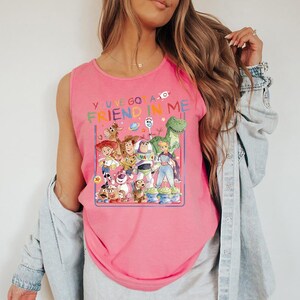 Pu&ograve; includere: Canotta rosa con una grafica colorata dei personaggi del film d'animazione "Toy Story". La grafica include Woody, Buzz Lightyear, Jessie e gli alieni, con la scritta "You've Got a Friend in Me."