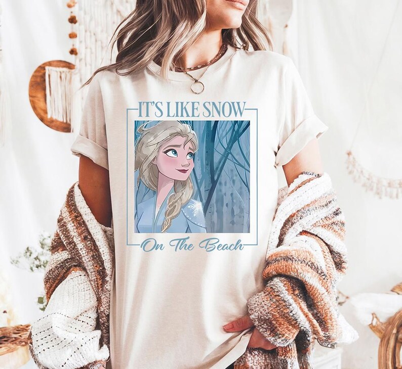 May include: White t-shirt with a graphic of Elsa from Frozen. The graphic says "It's Like Snow - On The Beach".