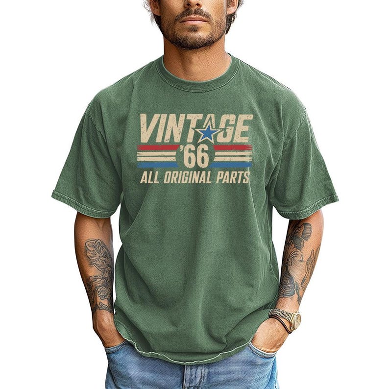 Puede incluir: Camiseta verde con el texto "VINTAGE '66 ALL ORIGINAL PARTS" en una fuente desgastada. El dise&ntilde;o incluye una estrella azul y rayas rojas y azules. La camiseta tiene mangas cortas y cuello redondo.