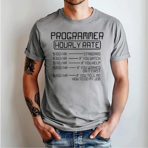 May include: A grey t-shirt featuring the text "PROGRAMMER HOURLY RATE" in black. The text includes hourly rates and conditions: standard, if you watch, if you help, if you worked on it first, and if you tell me how to do my job.