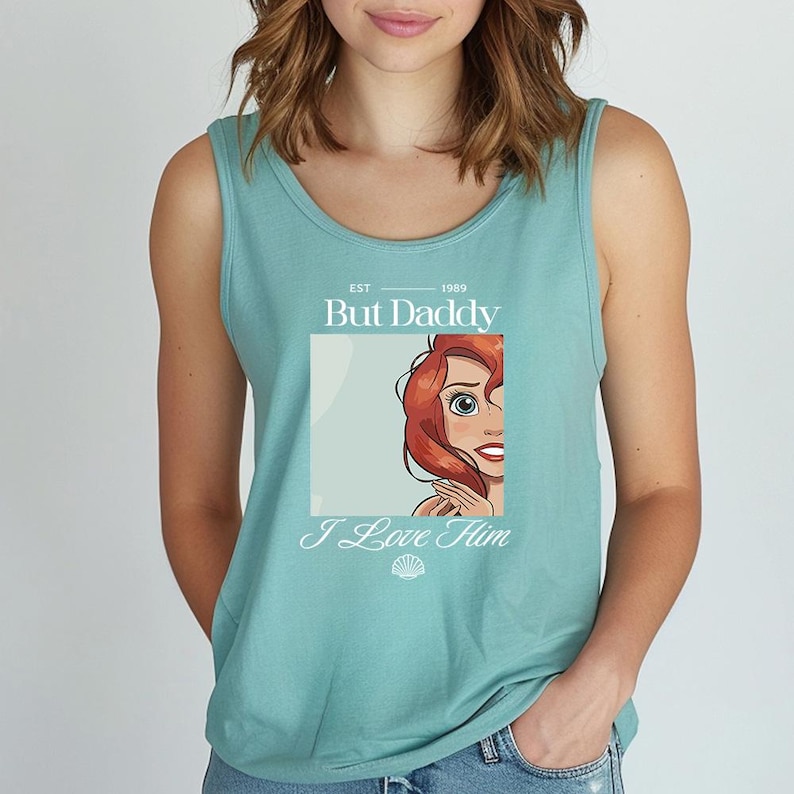 May include: A teal tank top with a graphic featuring a cartoon character with red hair. The text on the shirt reads "But Daddy I Love Him" with the year "1989" above the text.