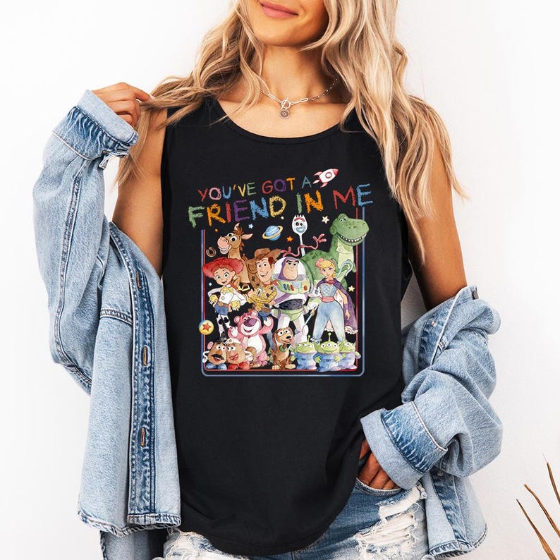 Pu&ograve; includere: Canotta nera con una grafica colorata dei personaggi del film "Toy Story". Il design include il testo "YOU'VE GOT A FRIEND IN ME" in colori arcobaleno, con un'icona a forma di razzo.