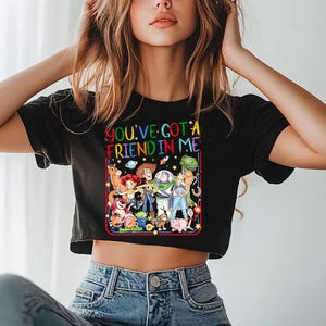 May include: A black short-sleeved t-shirt featuring a colorful graphic print of various animated characters from the Toy Story franchise. The text "YOU'VE GOT A FRIEND IN ME" is printed in multi-colored letters above the character group.