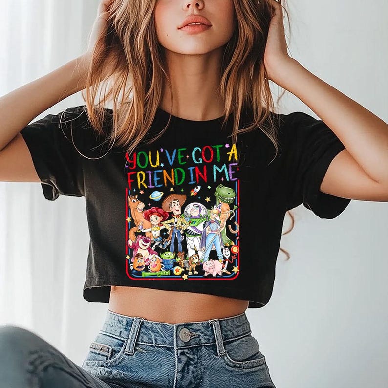 May include: A black short-sleeved t-shirt featuring a colorful graphic print of various animated characters from the Toy Story franchise. The text "YOU'VE GOT A FRIEND IN ME" is printed in multi-colored letters above the character group.