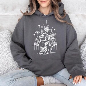 May include: A charcoal gray hooded sweatshirt featuring a white graphic of a cartoon character in front of a castle. The graphic includes fireworks and heart shapes. The sweatshirt has a front pocket and a drawstring hood.
