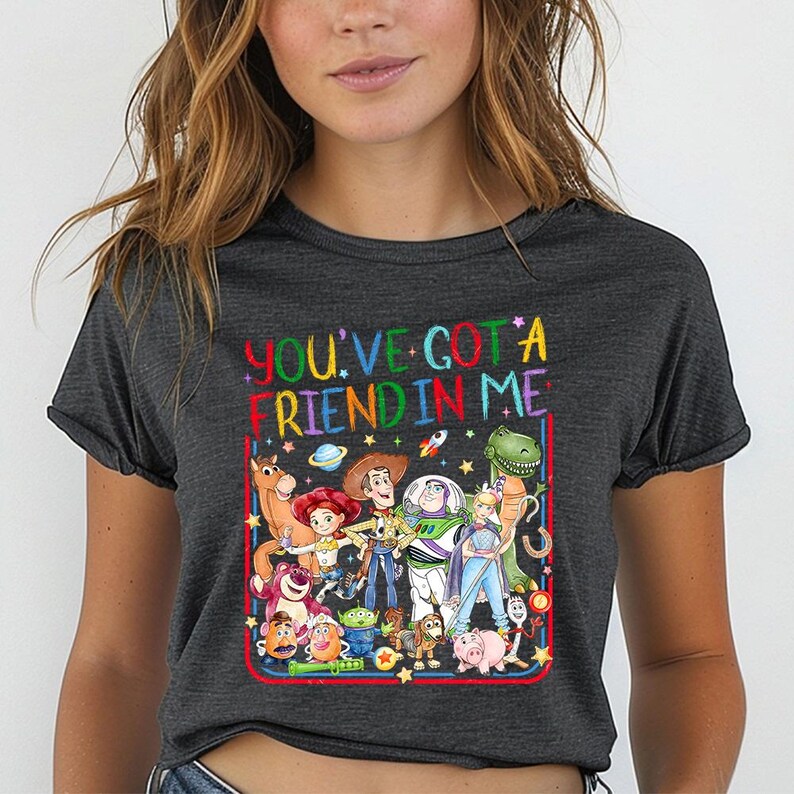 May include: A charcoal gray t-shirt featuring a colorful graphic print of various animated characters from the Toy Story franchise. The text "YOU'VE GOT A FRIEND IN ME" is printed in a multi-colored, rainbow-style font above the character group.