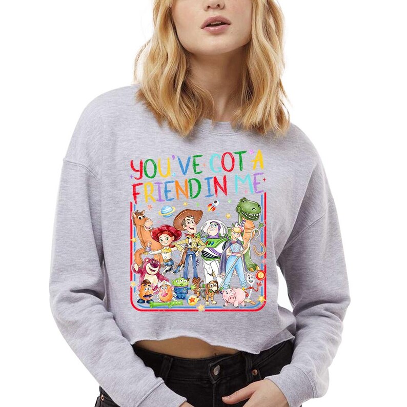 Peut inclure: Un sweat-shirt court gris clair avec une impression graphique color&eacute;e repr&eacute;sentant divers personnages de jouets anim&eacute;s. Au-dessus des personnages, le texte YOU'VE GOT A FRIEND IN ME est &eacute;crit en lettres multicolores. Le motif est bord&eacute; de rouge.