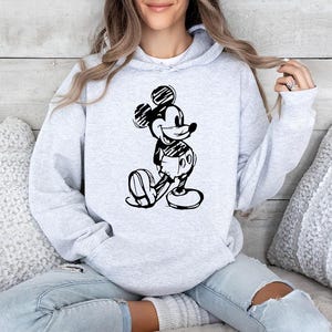 May include: A light gray hoodie featuring a black and white sketch of Mickey Mouse. The hoodie has a drawstring hood and a kangaroo pocket. The design is centered on the front of the sweatshirt.