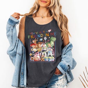 Pu&ograve; includere: Canotta grigio scuro con una grafica colorata di personaggi di un popolare film d'animazione. Il testo "YOU'VE GOT A FRIEND IN ME" &egrave; sopra la grafica. La canotta &egrave; senza maniche e realizzata in materiale morbido.