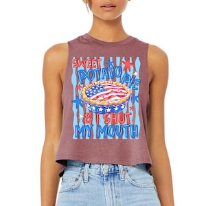 Op de afbeelding: Een mauve mouwloze crop top met een grafische print van een taart met een Amerikaanse vlagpatroon op de korst. De tekst SWEET POTATO PIE & I SHUT MY MOUTH staat in blauwe en rode letters, omringd door sterren en lichtblauwe strepen op de achtergrond.