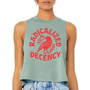 May include: Sage green crop top with a red graphic. The graphic features a bird holding a sprig and the words "RADICALIZED BY BASIC DECENCY" in a circular design. The top is sleeveless and made of a soft material.