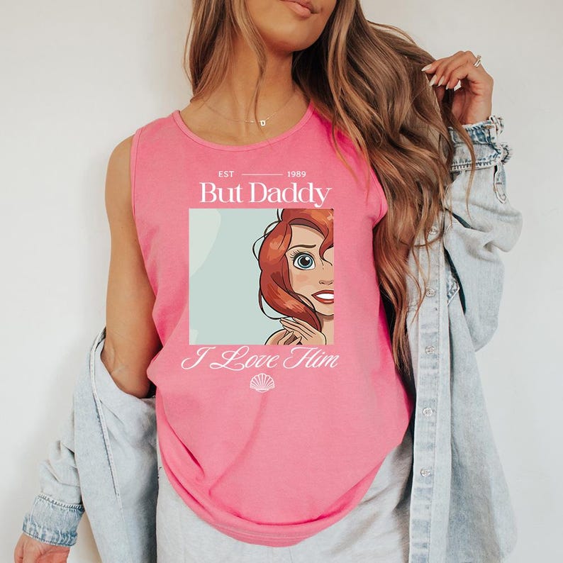 May include: Pink tank top with the text "But Daddy I Love Him" and a cartoon illustration of a red-haired character. The top has a scoop neck and is sleeveless.